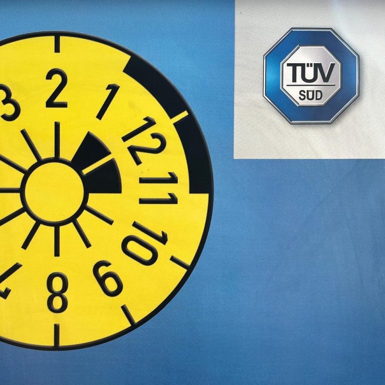 Ziffernrad mit gelbem Hintergrund und TÜV-Siegel oben rechts.