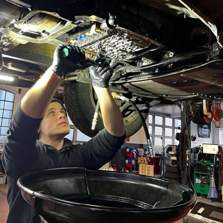 Junger Mechaniker arbeitet unter einem Auto und wechselt das Öl.